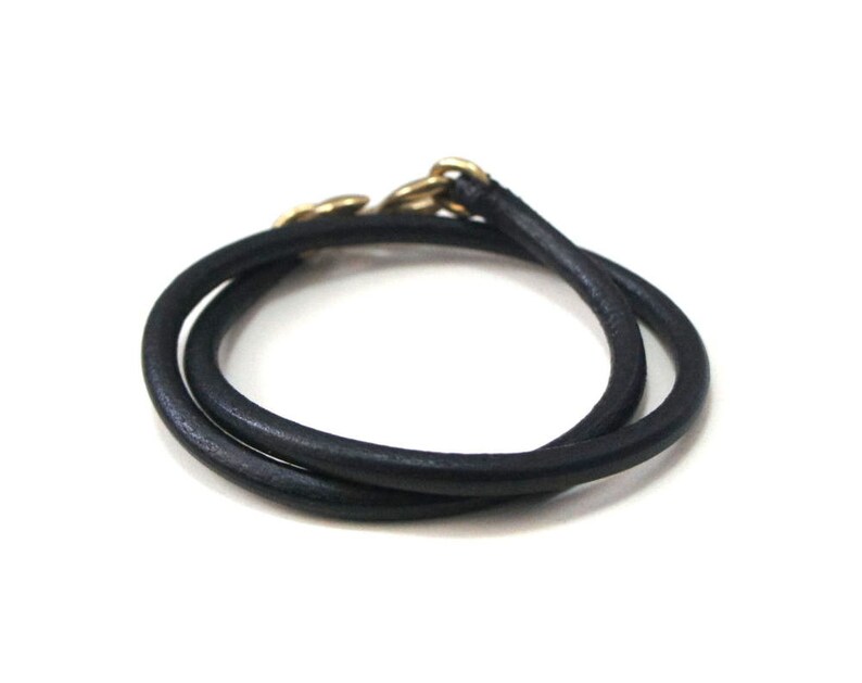 Puede incluir: Un brazalete de cuero negro con un cierre dorado.