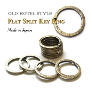 Op de afbeelding: Een set gespleten sleutelringen van messing met de woorden "Smoky Sumis Store" en "Old Valley Tokyo" erop gegraveerd. De sleutelringen zijn op elkaar gestapeld en zijn gemaakt in Japan.