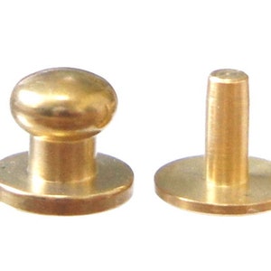 May include: Two gold-toned metal button snaps, one with a round head and the other with a flat head. Both have a flat base.