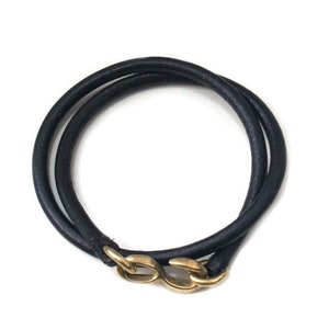 Puede incluir: Un brazalete de cuero negro con un cierre dorado. El brazalete est&aacute; envuelto dos veces y tiene un dise&ntilde;o simple y minimalista.