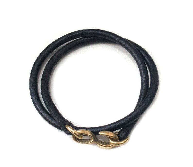 Puede incluir: Un brazalete de cuero negro con un cierre dorado. El brazalete est&aacute; envuelto dos veces y tiene un dise&ntilde;o simple y minimalista.