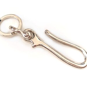 Op de afbeelding: Zilveren sleutelhanger met een ronde ring en een haak. De haak is gebogen.