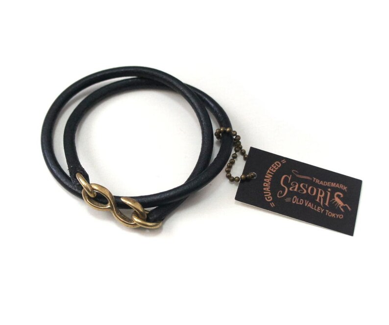 Puede incluir: Pulsera de cuero negro con cierre de s&iacute;mbolo de infinito de lat&oacute;n. La pulsera est&aacute; envuelta dos veces y tiene una peque&ntilde;a etiqueta adjunta que dice "Guaranteed - Sasori - Trademark - Old Valley Tokyo".