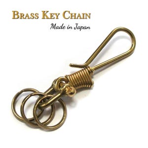 Op de afbeelding: Een messing sleutelhanger met drie kleine ringen en een sluiting. De sleutelhanger is goudkleurig en heeft de tekst "Brass Key Chain Made in Japan".