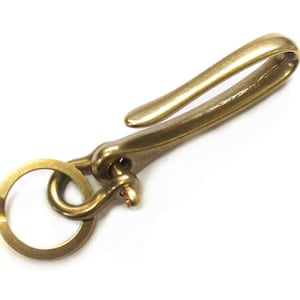 May include: A brass key chain with a hook and a ring. The hook is curved and the ring is round.