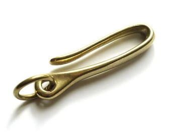 Könnte beinhalten: Ein Schlüsselanhängerhaken aus Messing mit einem glatten, geschwungenen Design. Der Haken hat an einem Ende einen kleinen Ring zum Anbringen von Schlüsseln oder anderen Gegenständen.