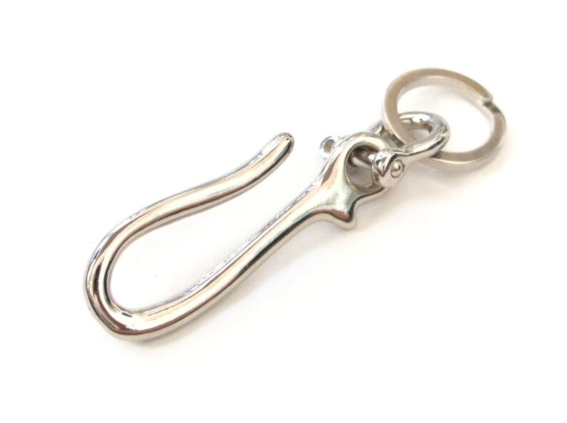 Op de afbeelding: Een zilveren sleutelhanger met een grote haak en een kleinere ring. De haak is gebogen en heeft een gladde afwerking.