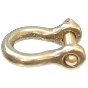 May include: A gold-colored metal shackle with a rounded, smooth surface and a pin through the center. The shackle is designed for attaching ropes or chains.