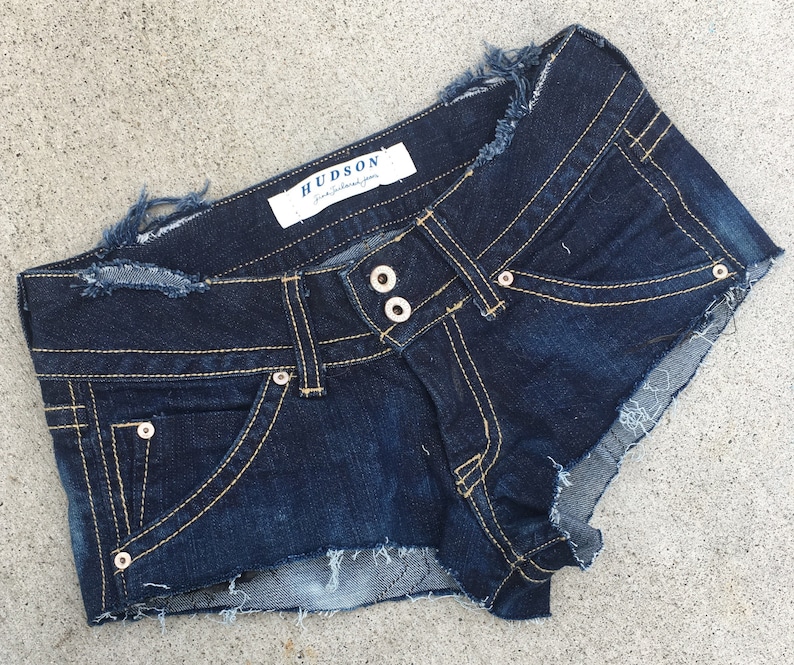 May include: Dark blue denim shorts with frayed edges and a small pocket on the front. The shorts have a label that reads "HUDSON -  jeans that fit you".