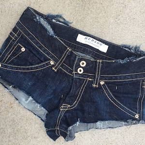 May include: Dark blue denim shorts with frayed edges and a Hudson brand label. The shorts have a single button and two belt loops.