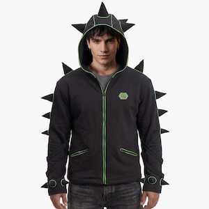 May include: Black zip-up hoodie with green trim and spiky accents. The hoodie features a hood with spikes, spikes along the spine, and wrist cuffs with spikes. A small green logo is on the chest. The hoodie is worn over a gray t-shirt.
