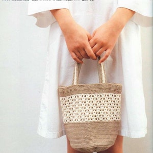 May include: A crocheted tote bag in brown and white. The bag has a wide, rectangular shape with a flat base and two handles. The bag is made with a simple stitch pattern and has a woven look.
