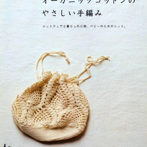 May include: A close-up of a crocheted drawstring bag made from organic cotton. The bag is a light beige colour and has a delicate, lacy pattern. The bag is lying on a white fabric surface.