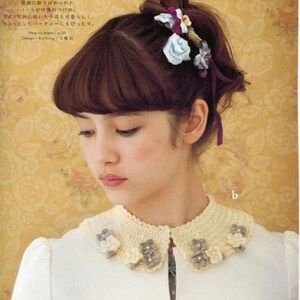 May include: A white crocheted collar with a scalloped edge and floral embellishments. The collar is decorated with small white and grey flowers.