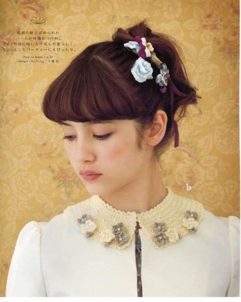 May include: A white crocheted collar with a scalloped edge and floral embellishments. The collar is decorated with small white and grey flowers.