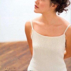 May include: A white crocheted camisole with a delicate lace trim. The camisole is sleeveless and has a scoop neck.