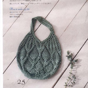 May include: A green crocheted tote bag with a pineapple stitch pattern. The bag is laying on a white wooden surface with a sprig of eucalyptus leaves.