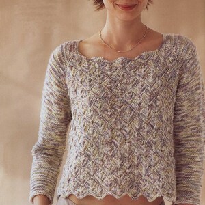 Könnte beinhalten: Ein helllila und cremefarbener Pullover mit einem gewellten Saum und einem quadratischen Ausschnitt. Der Pullover ist aus einem weichen, strukturierten Garn gefertigt.