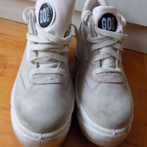 May include: Pair of light gray high-top sneakers with white soles and laces. The tongue of each shoe features a black and white circular logo with the word "GO" and "RIVOX". The sneakers are made of suede-like material.
