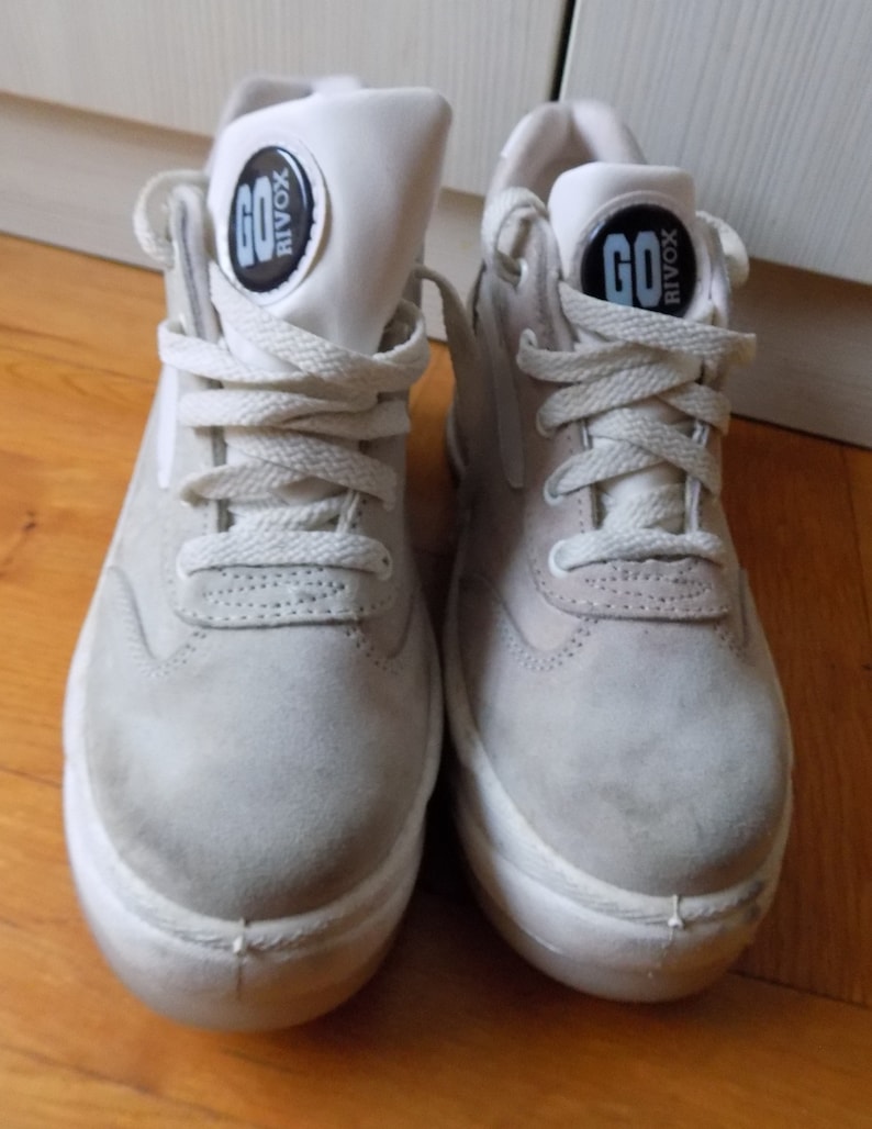 May include: Pair of light gray high-top sneakers with white soles and laces. The tongue of each shoe features a black and white circular logo with the word "GO" and "RIVOX". The sneakers are made of suede-like material.