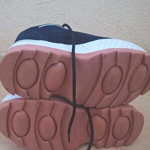 May include: A pair of athletic shoes with a navy blue upper, white midsole, and a thick, salmon-colored outsole. The shoes have black laces and a textured design on the sole.