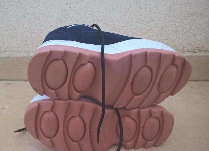 May include: A pair of athletic shoes with a navy blue upper, white midsole, and a thick, salmon-colored outsole. The shoes have black laces and a textured design on the sole.