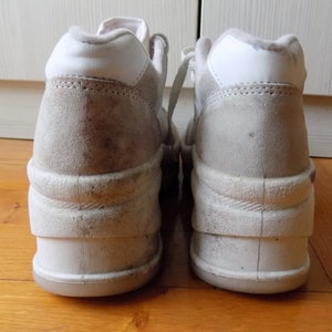 May include: Pair of off-white platform sneakers with a high-top design. The shoes feature a suede-like material on the upper and a thick, layered sole. The laces are white, and the shoes appear worn.