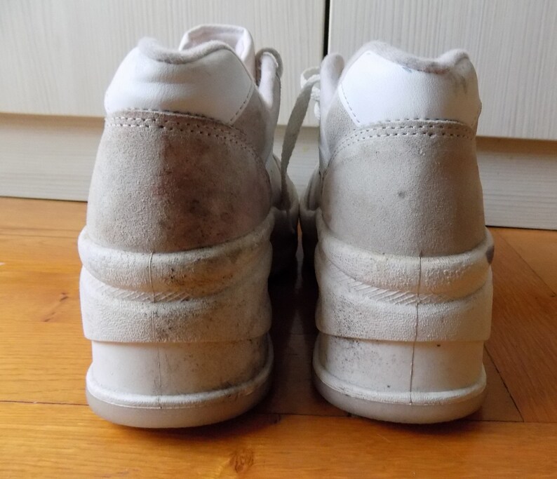 May include: Pair of off-white platform sneakers with a high-top design. The shoes feature a suede-like material on the upper and a thick, layered sole. The laces are white, and the shoes appear worn.