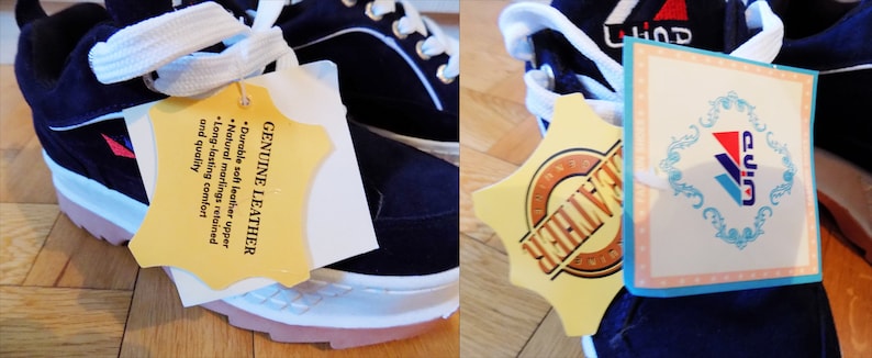 May include: Navy blue sneakers with white laces and soles. The shoes have a pink sole trim and a tag that reads "GENUINE LEATHER". The tag also lists features like "durable soft leather upper" and "long-lasting comfort".