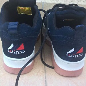 May include: Pair of navy blue sneakers with white and pink soles. The back of each shoe features a white, red, and blue logo with the word "Wind". Black laces are visible. The shoes appear to be unworn.