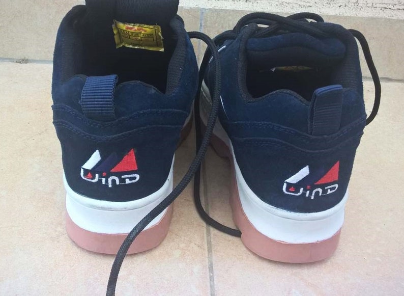 May include: Pair of navy blue sneakers with white and pink soles. The back of each shoe features a white, red, and blue logo with the word "Wind". Black laces are visible. The shoes appear to be unworn.