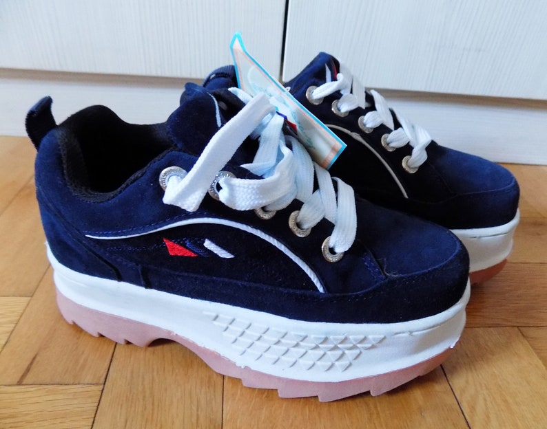May include: A pair of navy blue platform sneakers with white laces and a white sole. The sneakers have a pink outsole and a small red and white design on the side. The shoes are new and have a tag attached.