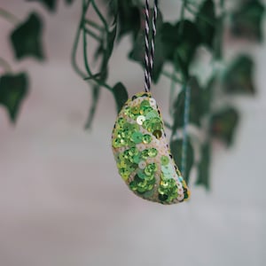 May include: A green and white lime-shaped ornament with sequins hanging from a string.