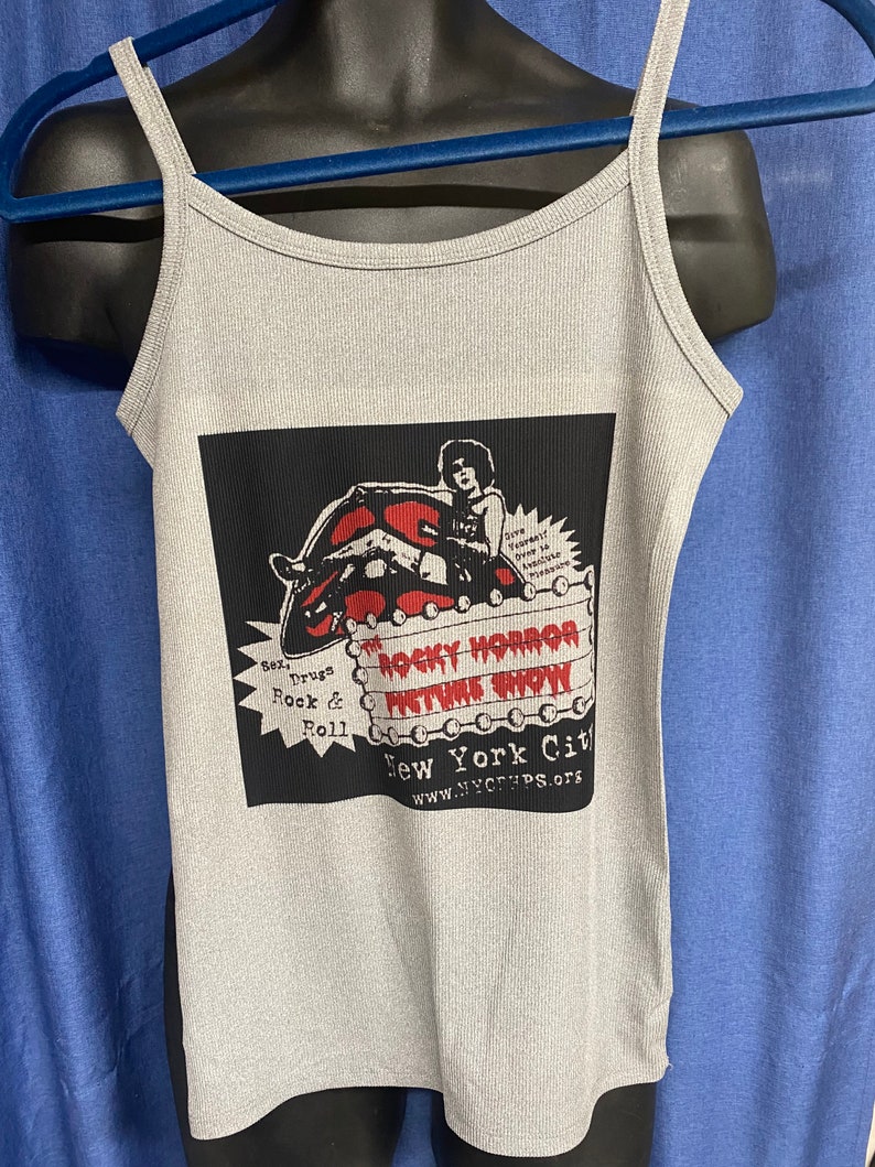 May include: A gray ribbed tank top with a graphic from "The Rocky Horror Picture Show." The graphic features a red lip design, the show's title, and the text "Sex, Drugs, Rock & Roll." The tank top has thin straps.