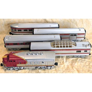 May include: A collection of model train cars, including a red and silver locomotive and several silver passenger cars with red stripes. The train cars are arranged on a light brown surface.