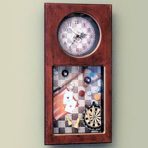 May include: A wooden wall clock with a round clock face and a smaller rectangular window below. The window shows a variety of game-themed items, including a chessboard, dice, playing cards, a dartboard, and a pool cue.