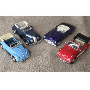 May include: Four toy convertible cars in various colors: light blue, dark blue, purple, and red. Each car has a detailed interior and open top. The cars are arranged on a textured, neutral-colored surface.