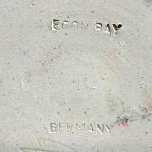 May include: Close-up of a white ceramic object with the words "Egon Bay Germany" stamped on the bottom.