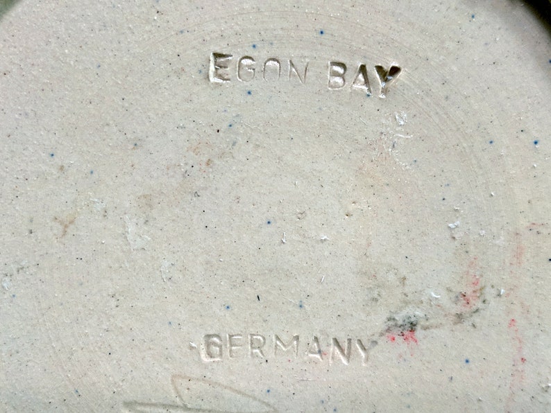May include: Close-up of a white ceramic object with the words "Egon Bay Germany" stamped on the bottom.