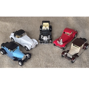 May include: A collection of five miniature vintage cars in various colors, including red, black, white, and blue. The toy cars have detailed features and are arranged on a neutral-colored surface.