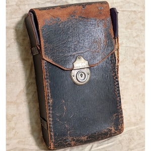 May include: A vintage leather camera case with a metal latch and a worn brown and black exterior.