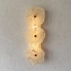 Peut inclure: Une applique murale verticale composée de trois disques translucides blanc cassé aux formes organiques disposés en colonne. Chaque disque présente une ouverture circulaire centrale avec un accent doré, diffusant une lueur douce et chaude.