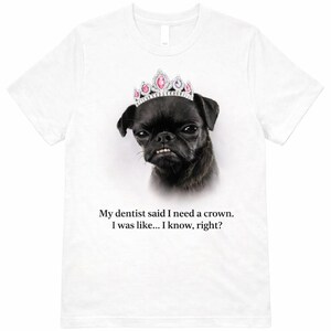 May include: White t-shirt featuring a black dog wearing a pink and silver crown. The text reads, "My dentist said I need a crown. I was like... I know, right?" A humorous design.