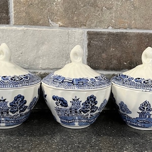 May include: Three blue and white porcelain lidded sugar bowls with a traditional willow pattern. The bowls are white with blue floral and geometric designs.