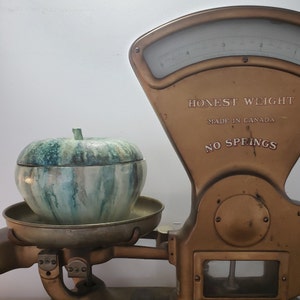 Peut inclure: Une balance en laiton vintage avec un récipient en céramique de forme de pomme vert et blanc sur la plateforme de pesage. La balance indique "Honest Weight Made in Canada No Springs".