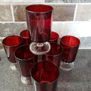 May include: Set of eight red glass tumblers with a clear glass stem. The glasses are stacked in a pyramid shape.