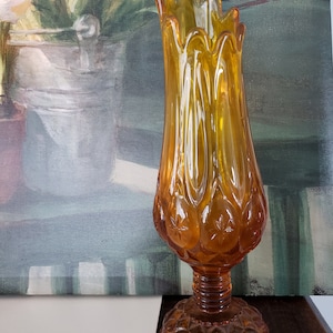 May include: Amber-colored glass vase with a starburst and scalloped design. The vase has a flared top and a pedestal base. The vase is approximately 10 inches tall.