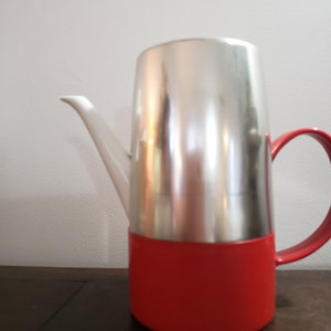 May include: A silver and red coffee pot with a white spout and a red handle.