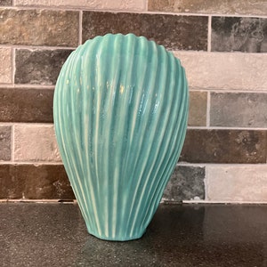 May include: A teal blue ceramic vase with a ribbed texture. The vase is shaped like a teardrop and has a smooth, glossy finish.