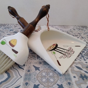 Peut inclure: Un ensemble balai et pelle en céramique blanche avec un manche en bois. La pelle a un motif de barbecue avec de la nourriture dessus. La brosse a un motif de verre de vin et un morceau de fromage.